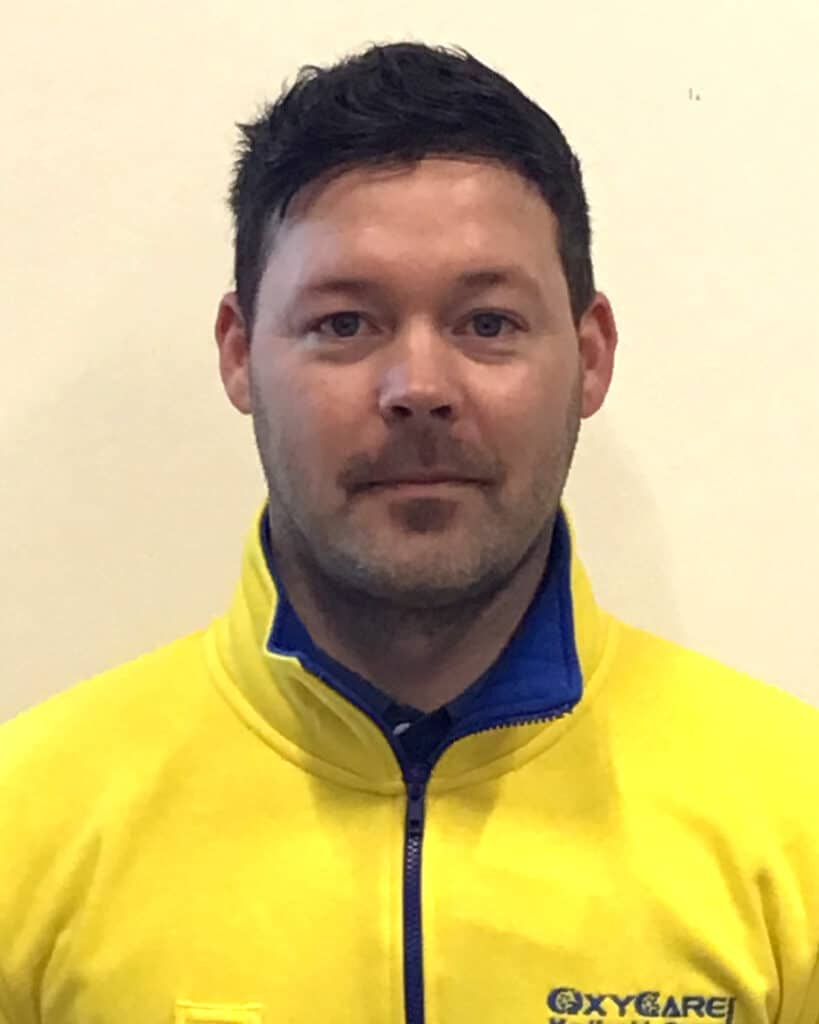 Foto von Fabrice Birgel, Mitarbeiter von OxyCare. Er trägt ein gelbes Hemd mit dem OxyCare Logo und schaut freundlich in die Kamera.