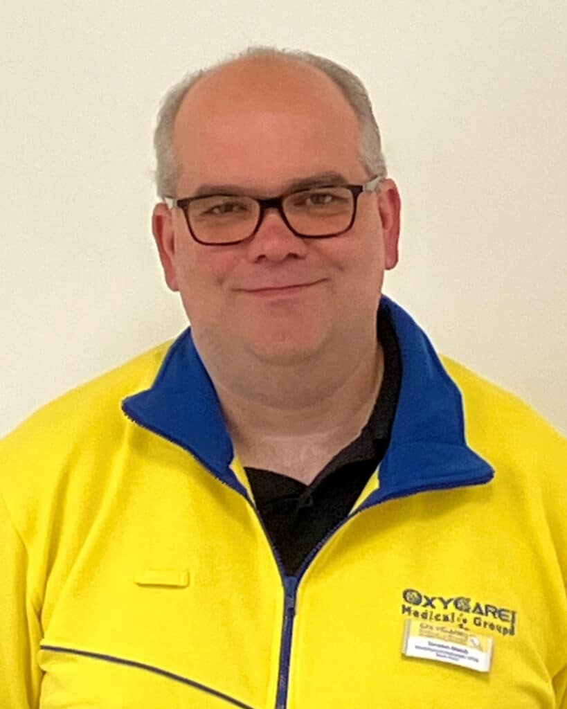 Foto von Torsten Bleich, Mitarbeiter von OxyCare. Er trägt ein gelbes Hemd mit dem OxyCare Logo und schaut freundlich in die Kamera.