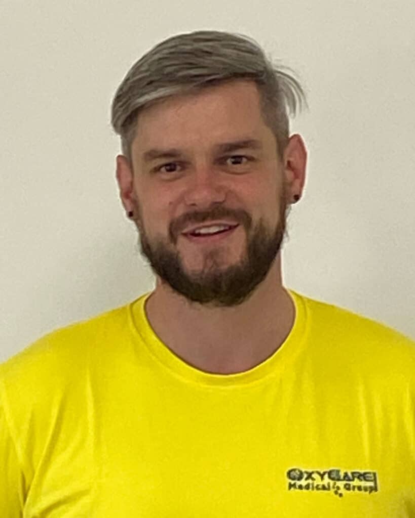 Foto von Martin Braun, Mitarbeiter von OxyCare. Er trägt ein gelbes Hemd mit dem OxyCare Logo und schaut freundlich in die Kamera.
