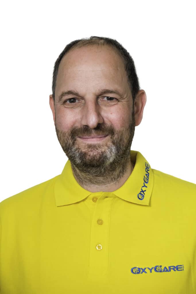 Foto von Christian Schlürscheid, Mitarbeiter von OxyCare. Er trägt ein gelbes Hemd mit dem OxyCare Logo und schaut freundlich in die Kamera.