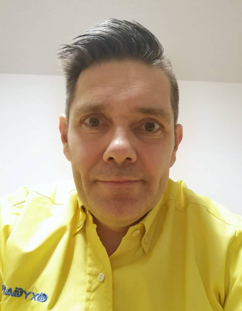 Foto von Raik Colberg, Mitarbeiter von OxyCare. Er trägt ein gelbes Hemd mit dem OxyCare Logo und schaut freundlich in die Kamera.