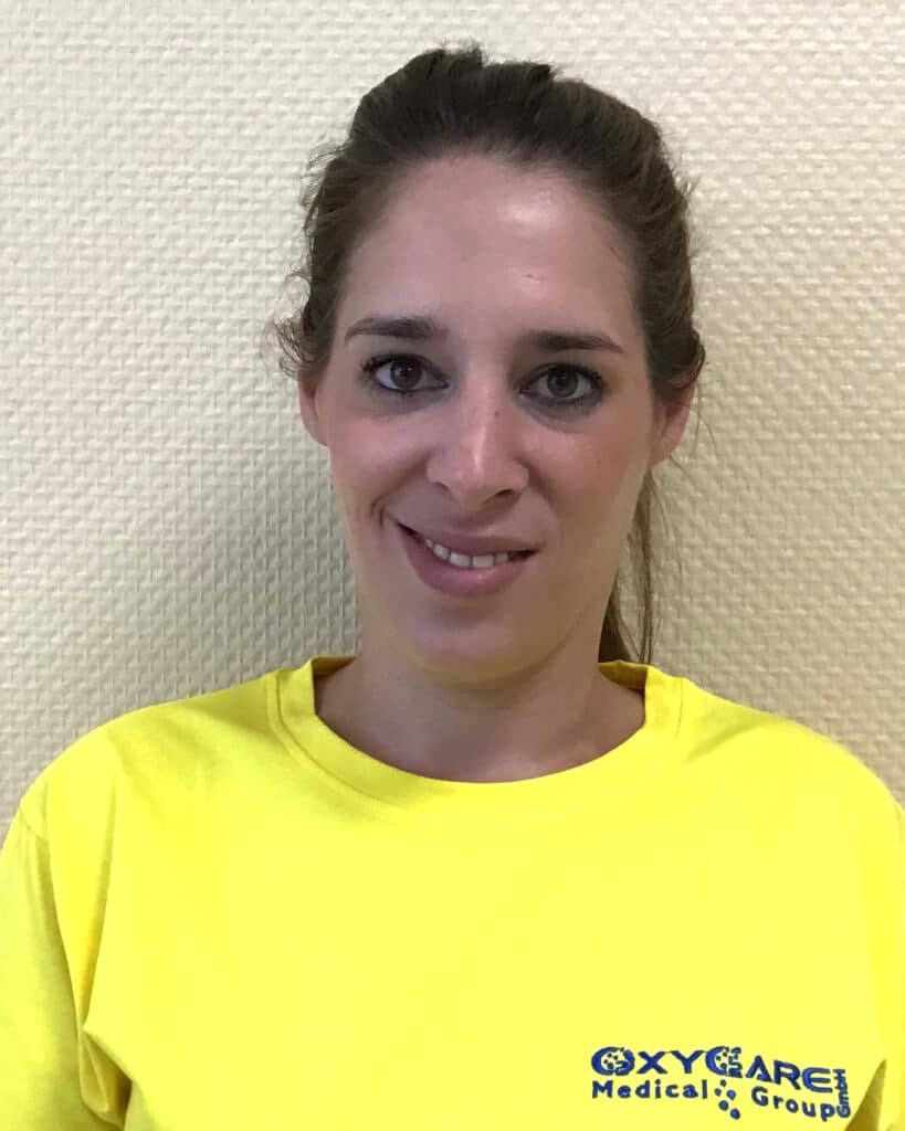 Foto von Kathrin Dillmann, Mitarbeiterin von OxyCare. Sie trägt ein gelbes Hemd mit dem OxyCare Logo und schaut freundlich in die Kamera.
