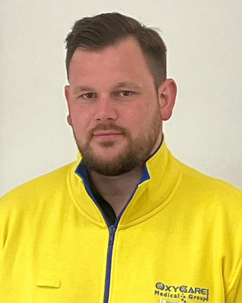 Foto von Marcel Dittert, Mitarbeiter von OxyCare. Er trägt ein gelbes Hemd mit dem OxyCare Logo und schaut freundlich in die Kamera.