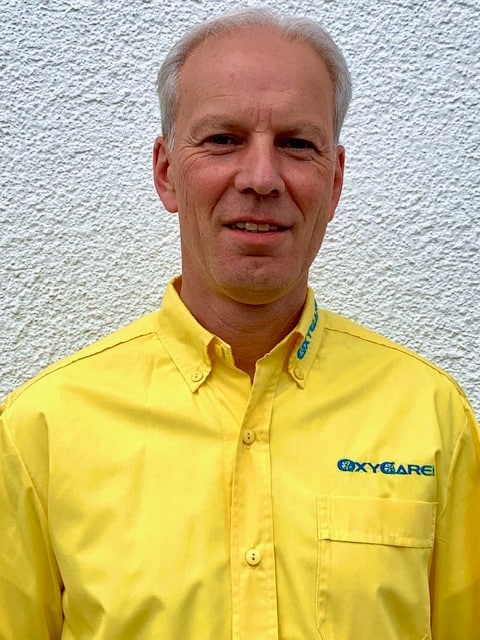 Foto von Dirk Filkorn, Mitarbeiter von OxyCare. Er trägt ein gelbes Hemd mit dem OxyCare Logo und schaut freundlich in die Kamera.