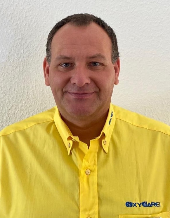 Foto von Michael Gall, Mitarbeiter von OxyCare. Er trägt ein gelbes Hemd mit dem OxyCare Logo und schaut freundlich in die Kamera.