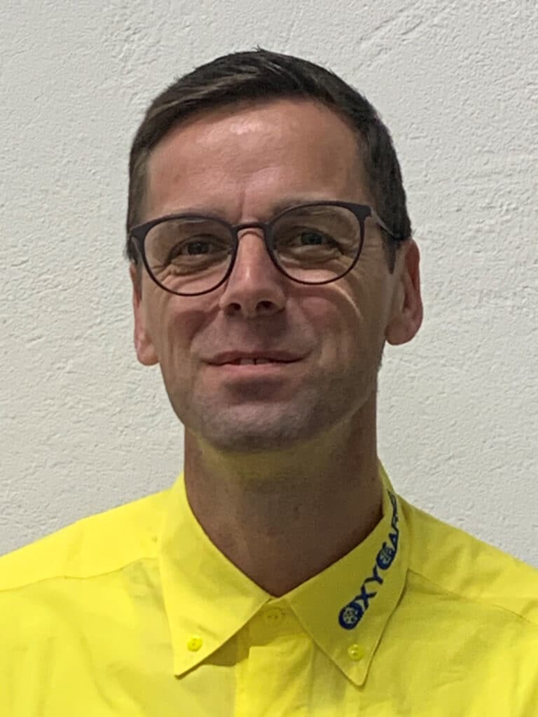 Foto von Steffen Heider, Mitarbeiter von OxyCare. Er trägt ein gelbes Hemd mit dem OxyCare Logo und schaut freundlich in die Kamera.
