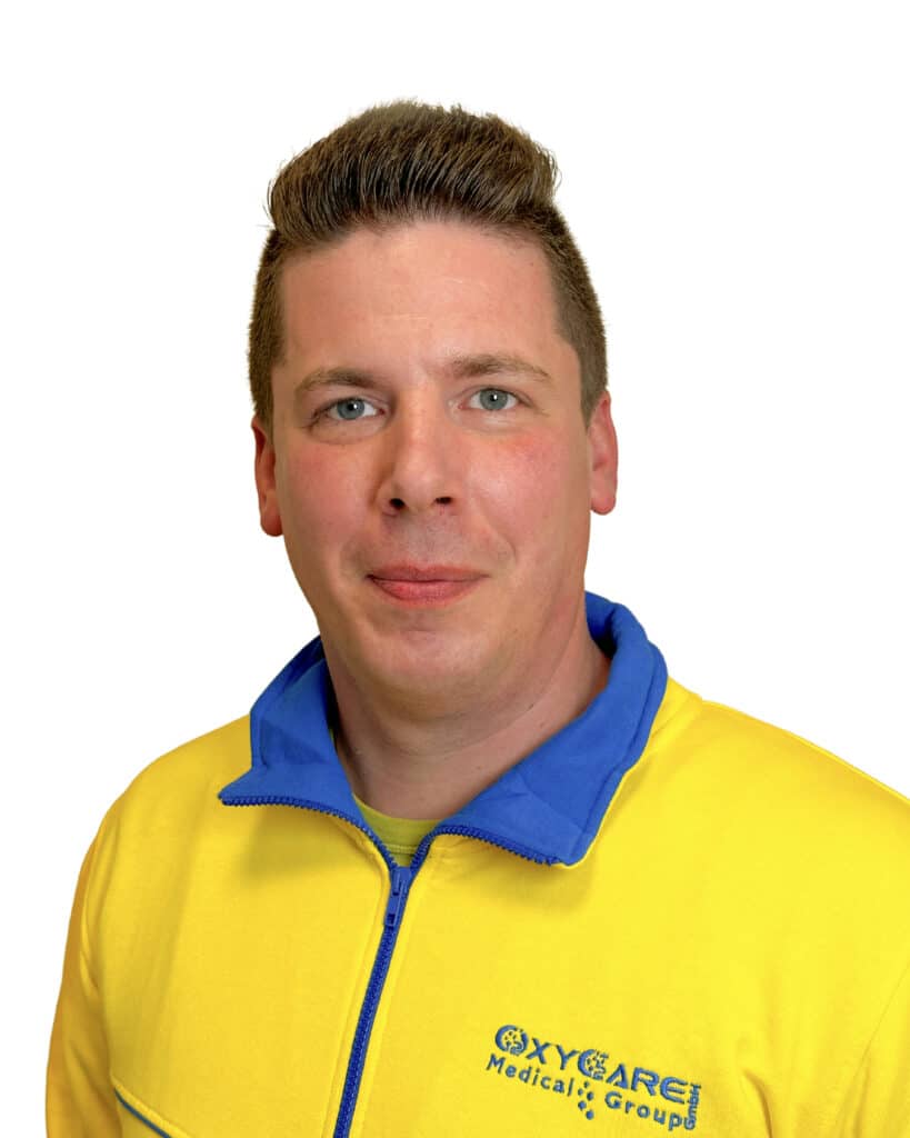Foto von Alexander Horn, Mitarbeiter von OxyCare. Er trägt ein gelbes Hemd mit dem OxyCare Logo und schaut freundlich in die Kamera.