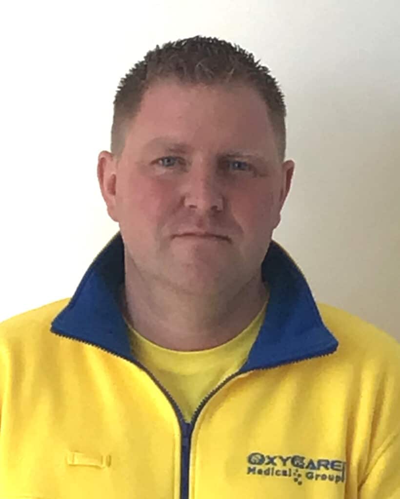 Foto von Mario Ihns, Mitarbeiter von OxyCare. Er trägt ein gelbes Hemd mit dem OxyCare Logo und schaut freundlich in die Kamera.