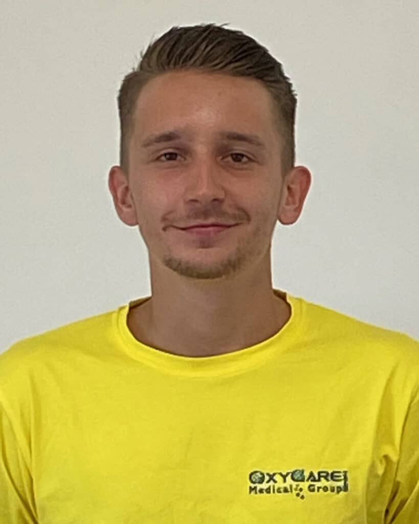 Foto von Leonard Jahn, Mitarbeiter von OxyCare. Er trägt ein gelbes Hemd mit dem OxyCare Logo und schaut freundlich in die Kamera.