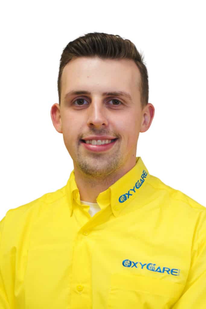 Foto von Jan Praschl, Mitarbeiter von OxyCare. Er trägt ein gelbes Hemd mit dem OxyCare Logo und schaut freundlich in die Kamera.