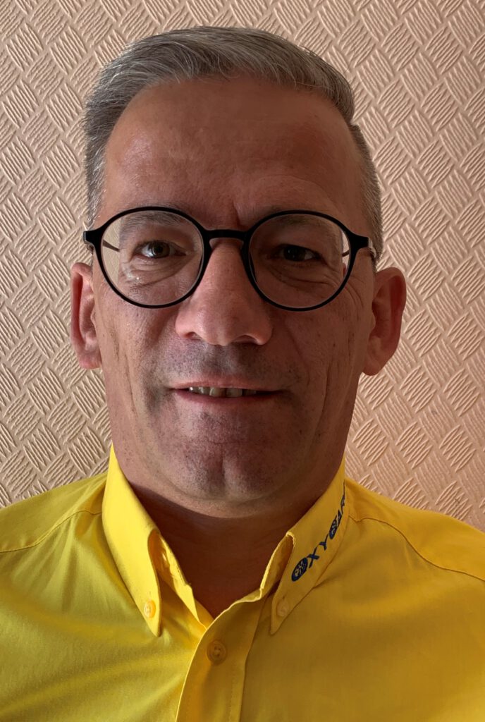 Foto von Volker Janka, Mitarbeiter von OxyCare. Er trägt ein gelbes Hemd mit dem OxyCare Logo und schaut freundlich in die Kamera.