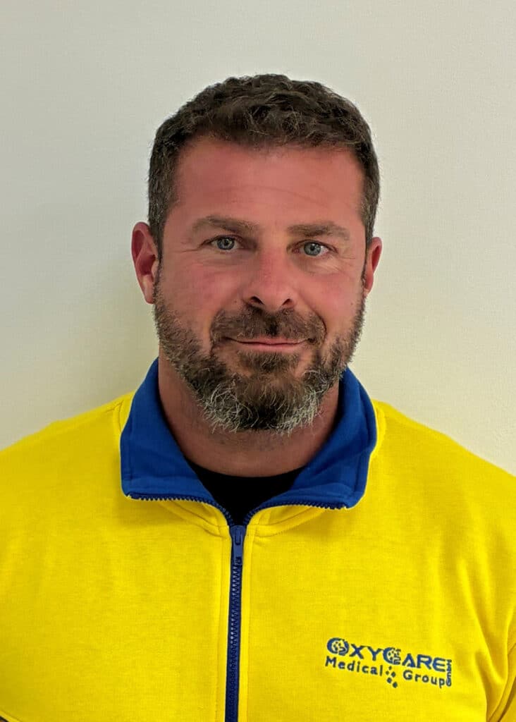 Foto von Tim Kalke, Mitarbeiter von OxyCare. Er trägt ein gelbes Hemd mit dem OxyCare Logo und schaut freundlich in die Kamera.
