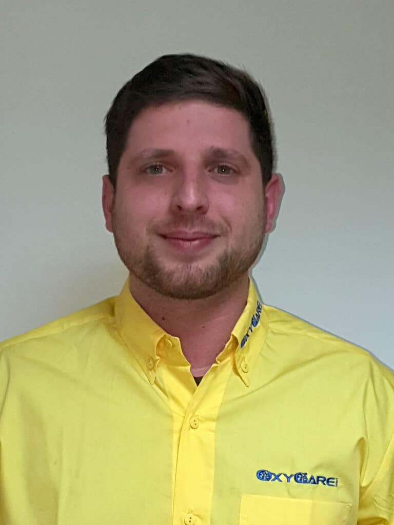Foto von Thomas Kindermann, Mitarbeiter von OxyCare. Er trägt ein gelbes Hemd mit dem OxyCare Logo und schaut freundlich in die Kamera.