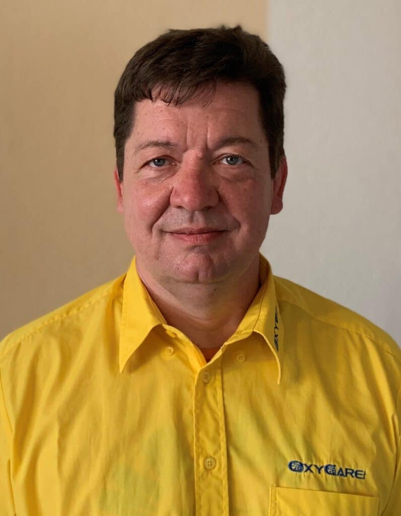 Foto von Marko Kranz, Mitarbeiter von OxyCare. Er trägt ein gelbes Hemd mit dem OxyCare Logo und schaut freundlich in die Kamera.