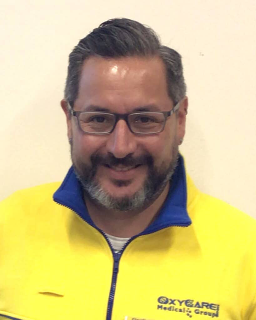 Foto von Josef Alexander Kreis, Mitarbeiter von OxyCare. Er trägt ein gelbes Hemd mit dem OxyCare Logo und schaut freundlich in die Kamera.