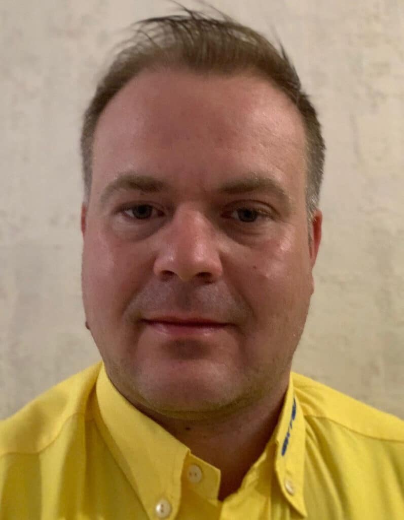 Foto von Henner Kruhm, Mitarbeiter von OxyCare. Er trägt ein gelbes Hemd mit dem OxyCare Logo und schaut freundlich in die Kamera.