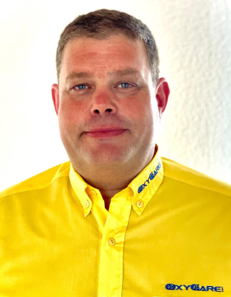 Foto von Thorsten Laschke, Mitarbeiter von OxyCare. Er trägt ein gelbes Hemd mit dem OxyCare Logo und schaut freundlich in die Kamera.
