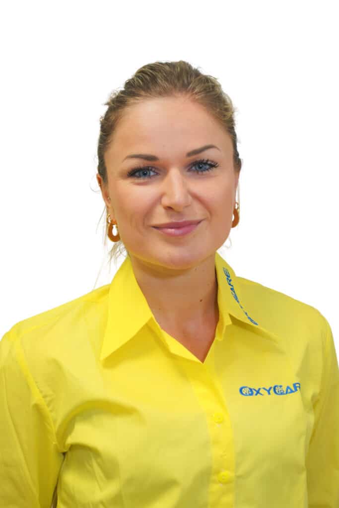 Foto von Linda Henneberger, Mitarbeiterin von OxyCare. Sie trägt ein gelbes Hemd mit dem OxyCare Logo und schaut freundlich in die Kamera.