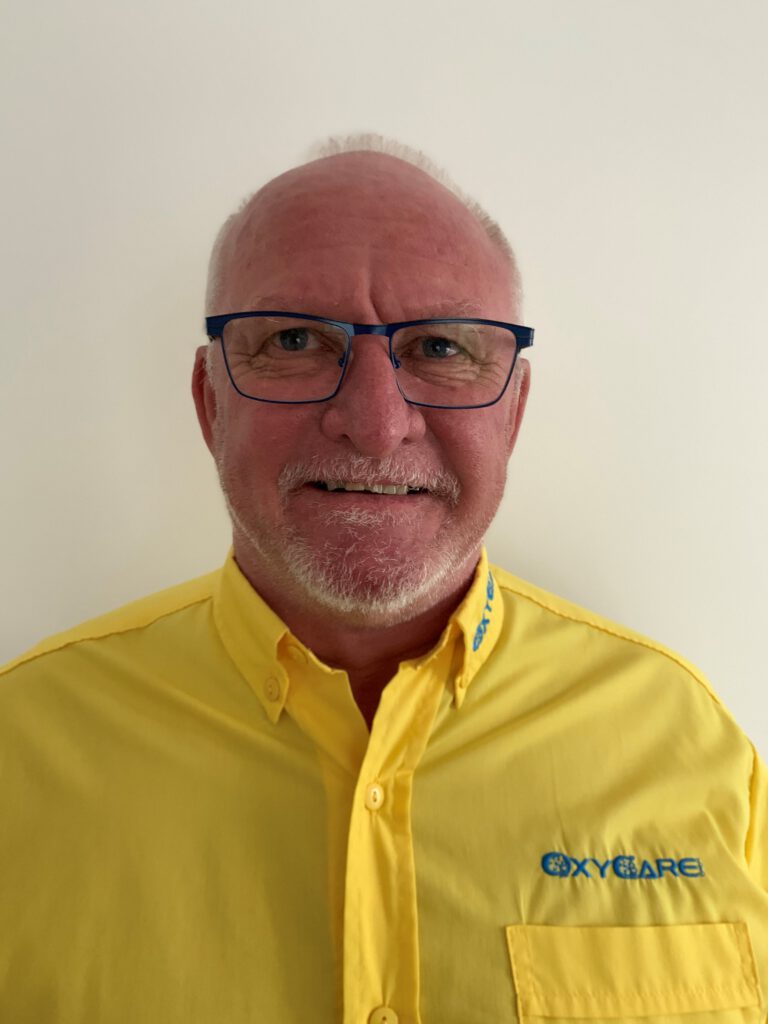 Foto von Thomas Mauerer, Mitarbeiter von OxyCare. Er trägt ein gelbes Hemd mit dem OxyCare Logo und schaut freundlich in die Kamera.