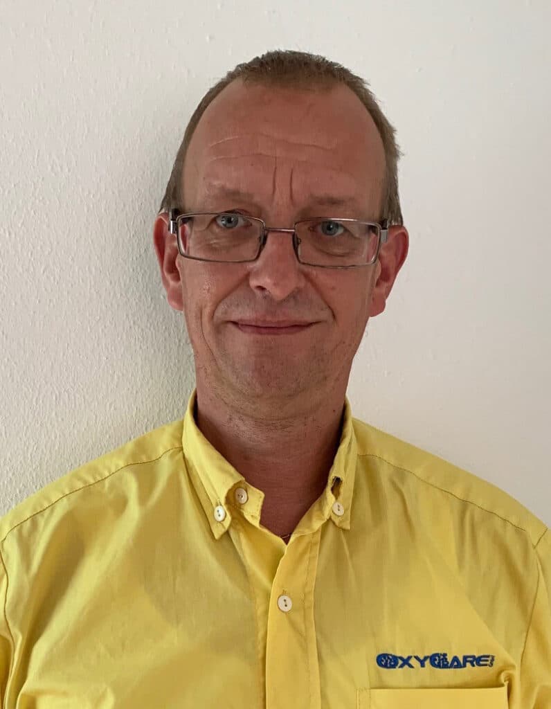 Foto von Mathias Meißner, Mitarbeiter von OxyCare. Er trägt ein gelbes Hemd mit dem OxyCare Logo und schaut freundlich in die Kamera.