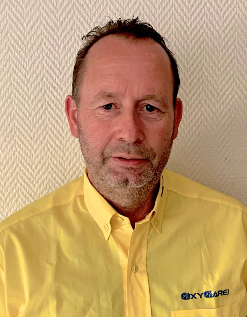 Foto von Thomas Peter Deuster, Mitarbeiter von OxyCare. Er trägt ein gelbes Hemd mit dem OxyCare Logo und schaut freundlich in die Kamera.