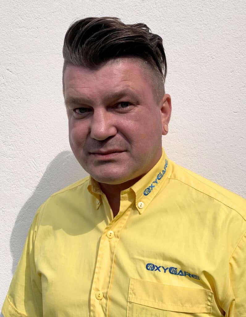 Foto von Sandro Richter, Mitarbeiter von OxyCare. Er trägt ein gelbes Hemd mit dem OxyCare Logo und schaut freundlich in die Kamera.