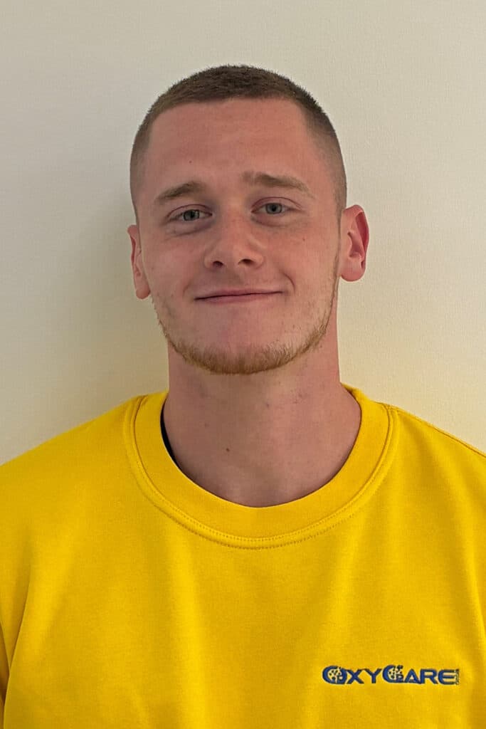Foto von Jeremy Roll, Mitarbeiter von OxyCare. Er trägt ein gelbes Hemd mit dem OxyCare Logo und schaut freundlich in die Kamera.