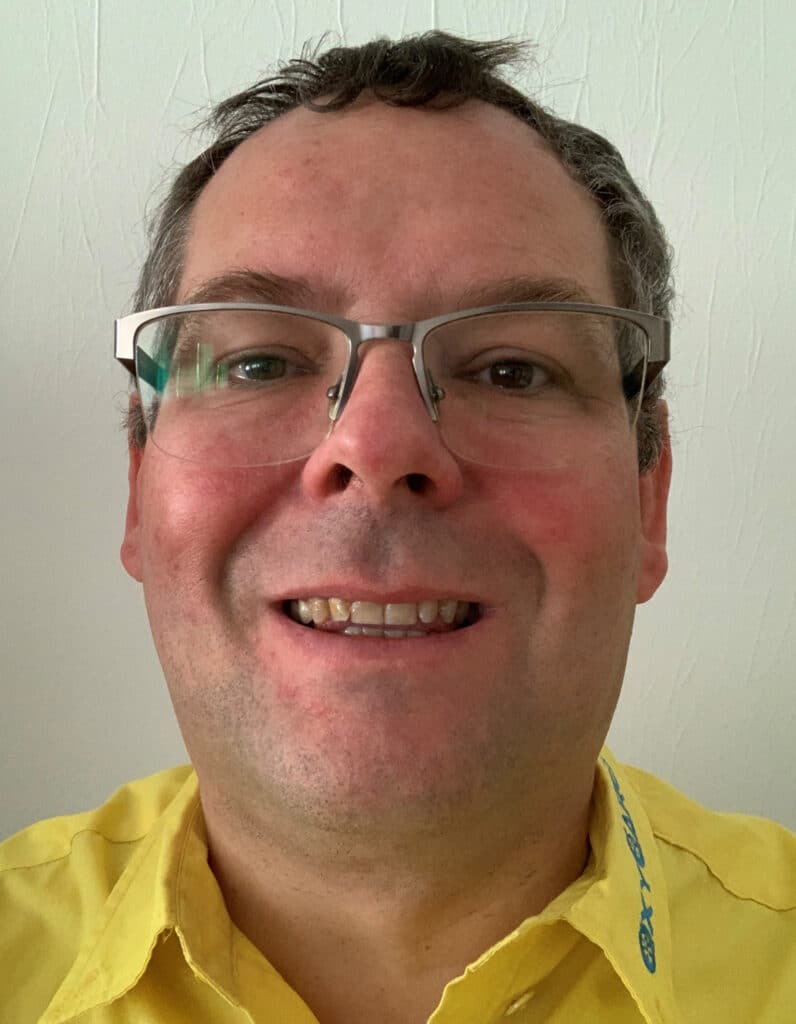 Foto von Knud Roloff, Mitarbeiter von OxyCare. Er trägt ein gelbes Hemd mit dem OxyCare Logo und schaut freundlich in die Kamera.