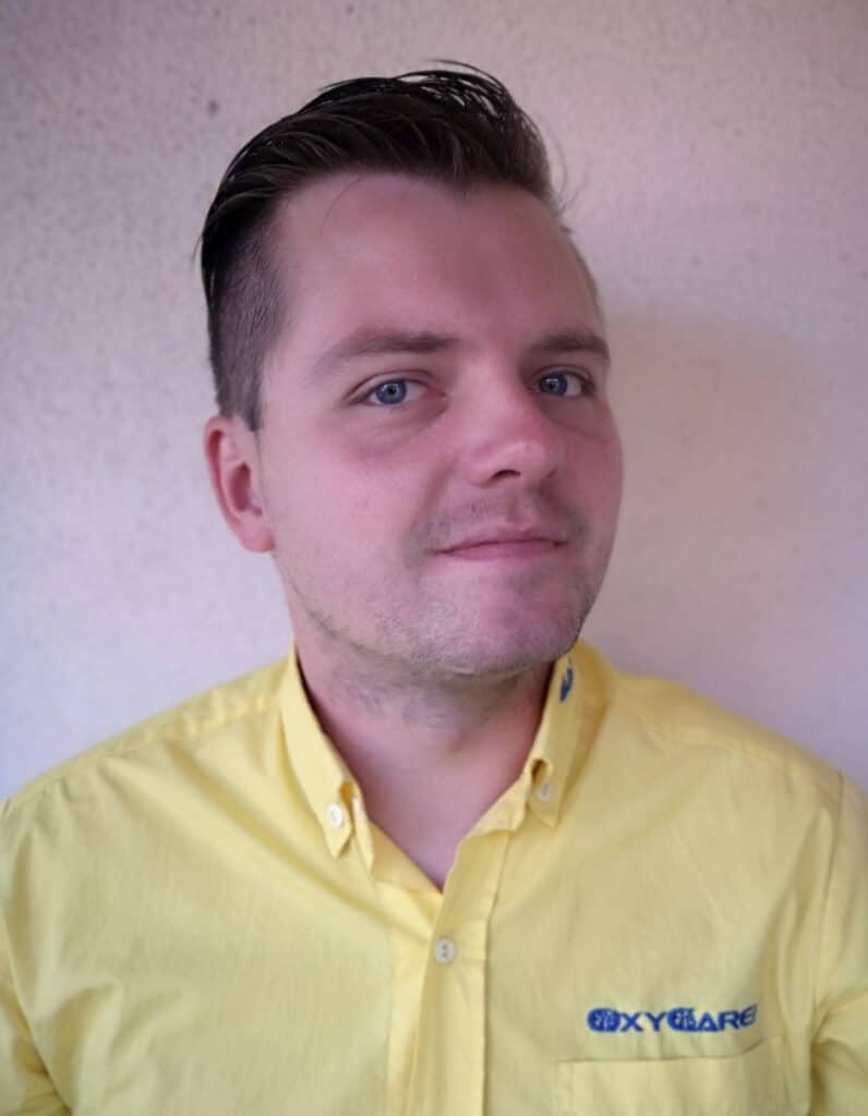 Foto von David Schmidt, Mitarbeiter von OxyCare. Er trägt ein gelbes Hemd mit dem OxyCare Logo und schaut freundlich in die Kamera.