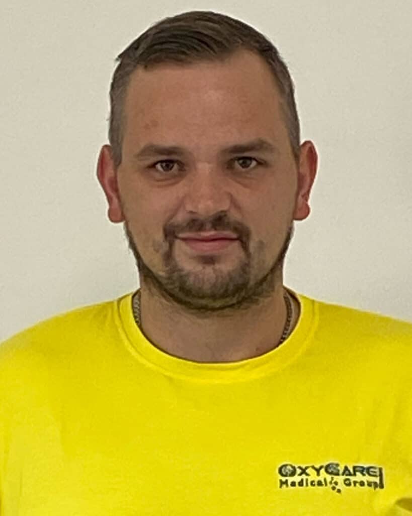 Foto von Fabian Schmidt, Mitarbeiter von OxyCare. Er trägt ein gelbes Hemd mit dem OxyCare Logo und schaut freundlich in die Kamera.