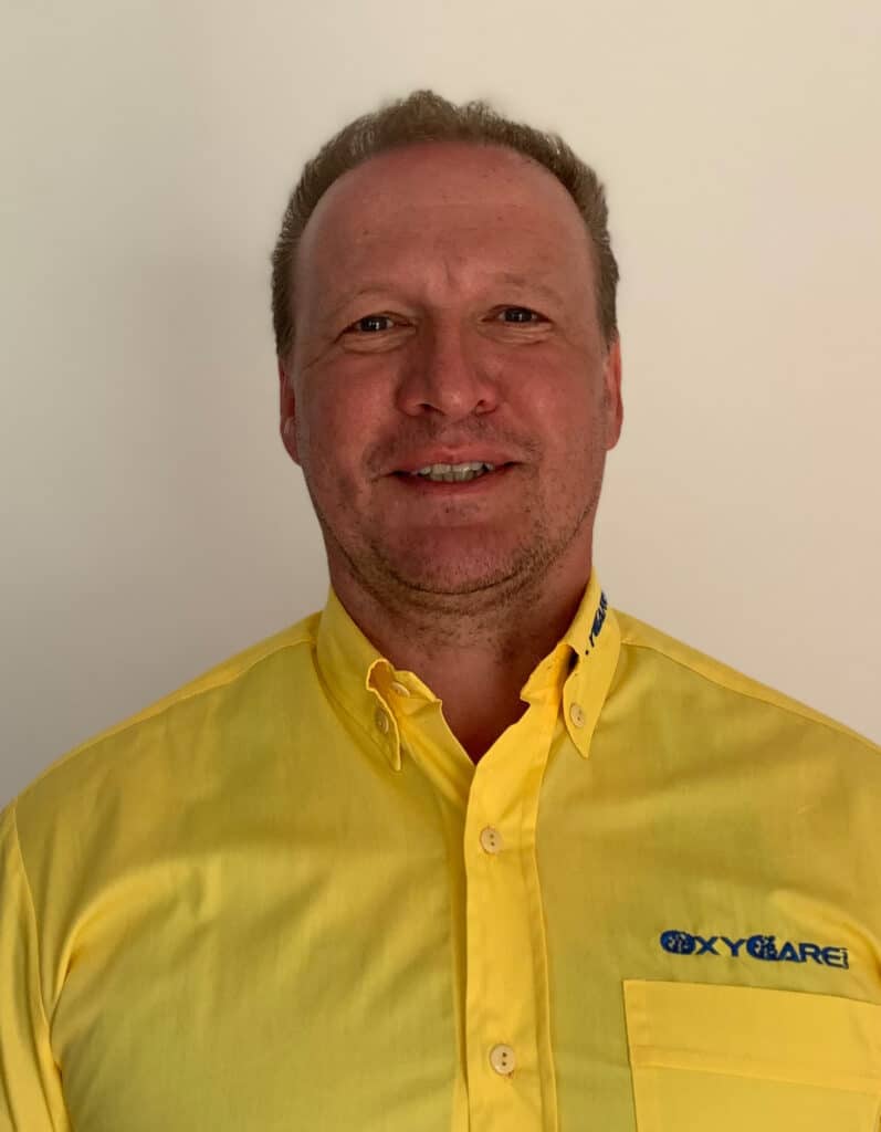 Foto von Markus Seth, Mitarbeiter von OxyCare. Er trägt ein gelbes Hemd mit dem OxyCare Logo und schaut freundlich in die Kamera.