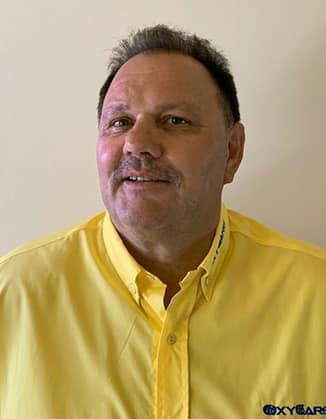 Foto von Werner Skrzeba, Mitarbeiter von OxyCare. Er trägt ein gelbes Hemd mit dem OxyCare Logo und schaut freundlich in die Kamera.