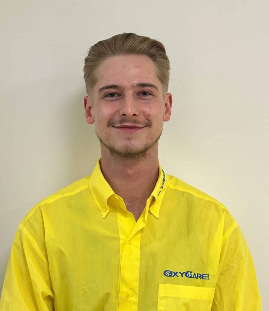 Foto von Thomas Wagner, Mitarbeiter von OxyCare. Er trägt ein gelbes Hemd mit dem OxyCare Logo und schaut freundlich in die Kamera.