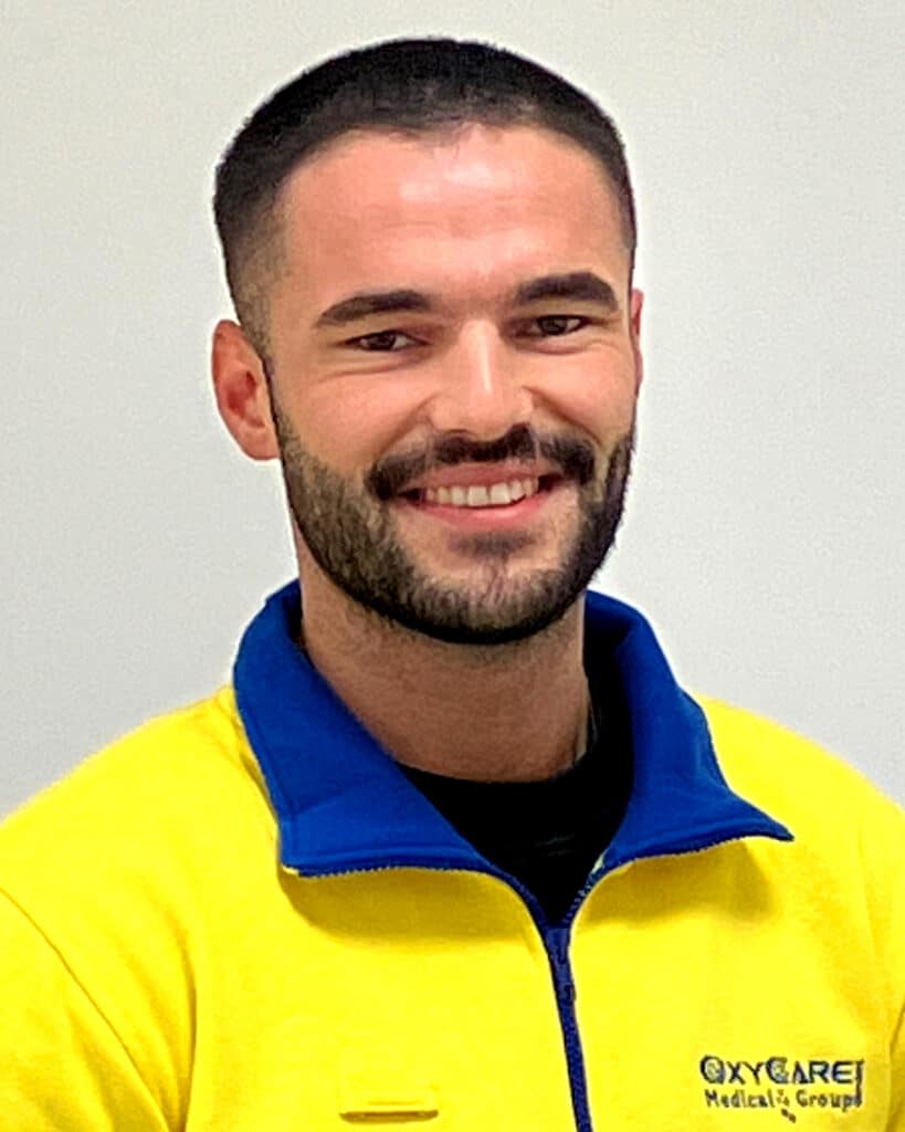 Foto von Ahmet Yildirim, Mitarbeiter von OxyCare. Er trägt ein gelbes Hemd mit dem OxyCare Logo und schaut freundlich in die Kamera.