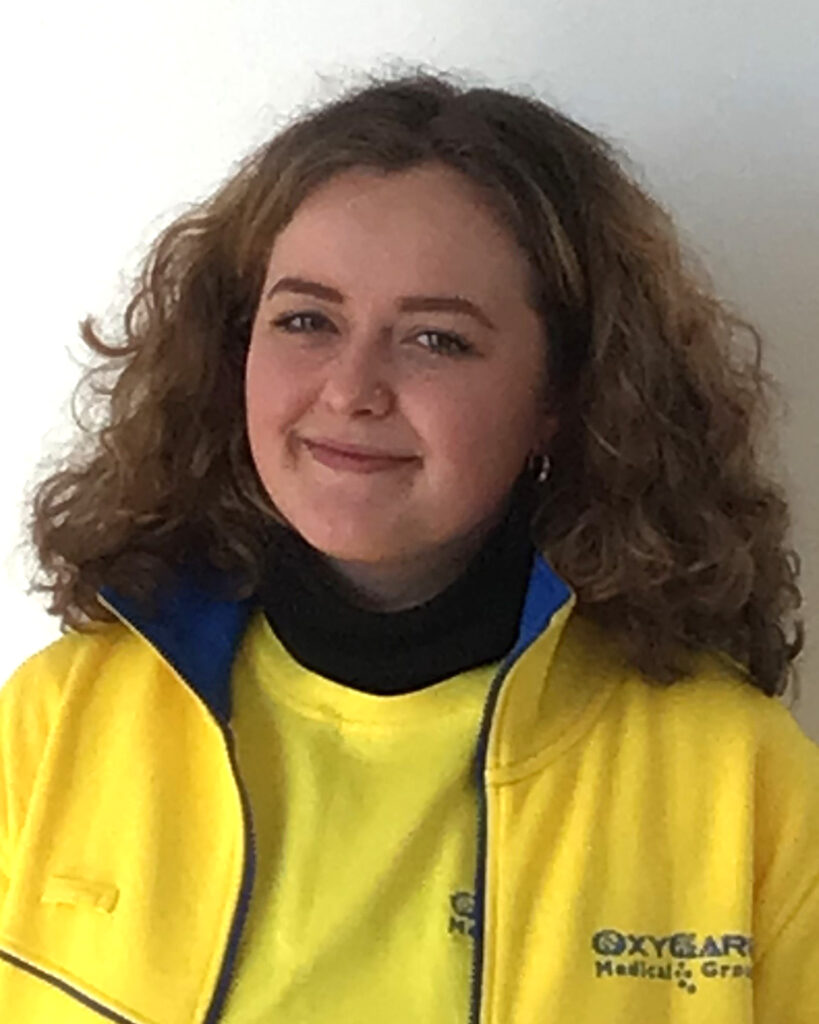 Foto von Julia Jundt, Mitarbeiterin von OxyCare. Sie trägt ein gelbes Hemd mit dem OxyCare Logo und schaut freundlich in die Kamera.