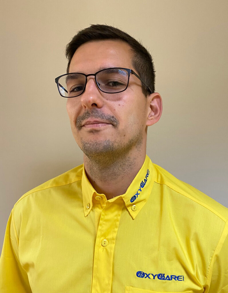 Foto von Toni Sill, Mitarbeiter von OxyCare. Er trägt ein gelbes Hemd mit dem OxyCare Logo und schaut freundlich in die Kamera.