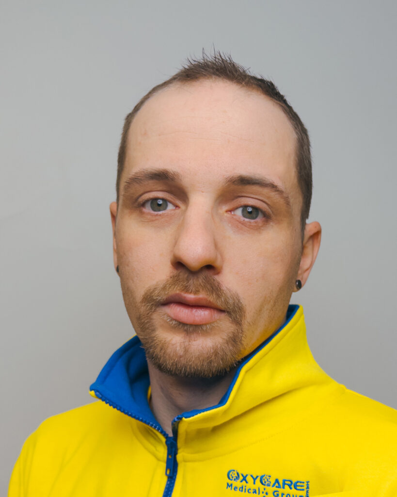 Foto von Vincent Reichardt, Mitarbeiter von OxyCare. Er trägt ein gelbes Hemd mit dem OxyCare Logo und schaut freundlich in die Kamera.